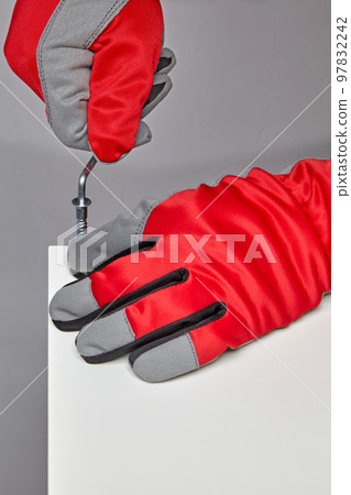Furniture assembler in red gloves is screwing in a screw with a hex wrench 97832242
