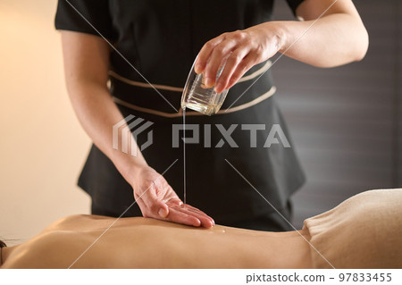 Esthetician dripping oil on the back at the beauty salon Esthetician dripping oil on the back at the beauty salon 97833455