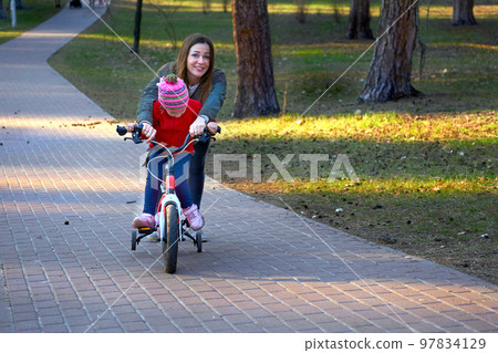 Cheerful mom teaches her child to ride a bike in autumn spring park 97834129