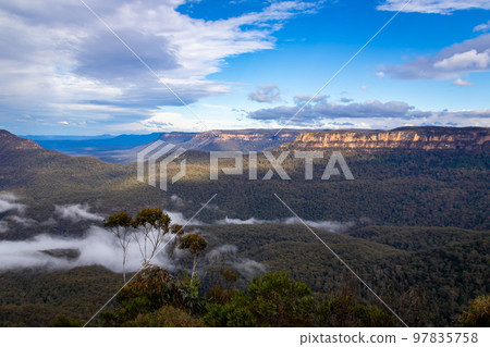 A forest with a slight sea of clouds and clouds floating in the blue sky seen in the Blue Mountains on the outskirts of Sydney 97835758