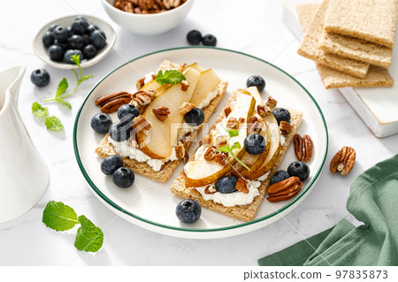 Crispbread with cream cheese, sweet pears, blueberry and pecan nuts. Top view 97835873