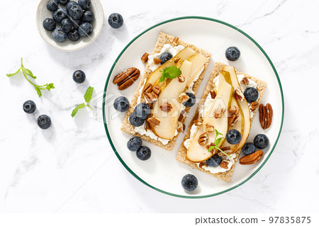 Crispbread with cream cheese, sweet pears, blueberry and pecan nuts. Top view 97835875