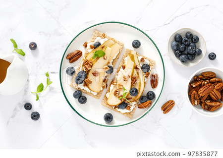 Crispbread with cream cheese, sweet pears, blueberry and pecan nuts. Top view 97835877