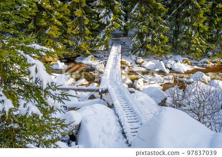 Small wooden footbridge covered by snow over icy mountain river in wintertime. 97837039