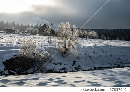 Wintertime landscape of Jizera Mountains. Snowy meadows and old wooden house on cold winter day. Jizerka, Czech Republic. Wintertime landscape of Jizera Mountains. Snowy meadows and old wooden house on cold winter day. Jizerka, Czech Republic. 97837041