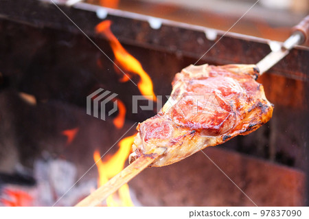 Beef steak on skewer on grill, flames on background. Barbecue in open air. Traditional meat cooking. 97837090
