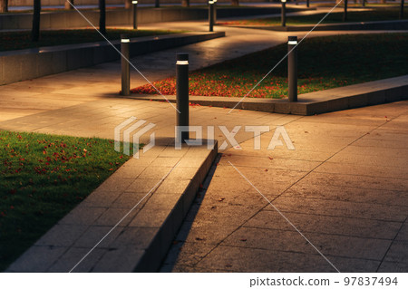 Row Of Outdoor Landscape Hard Paving Light. Lighting element on the green lawn along the footpath. Modern lighting system in landscape design. 97837494