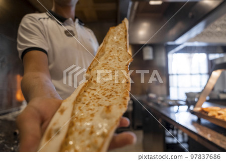 Midsection of male chef holding freshly baked Turkish cheese pide in commercial kitchen at restaurant 97837686