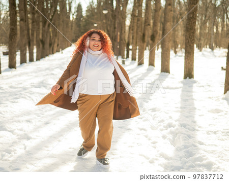 A fat woman listens to music with headphones and dances in the park in winter.  97837712