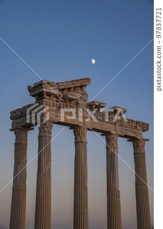 Low angle view of old ruins of Temple of Apollo with moon in clear blue sky in the background at dusk in Side, Turkey 97837721