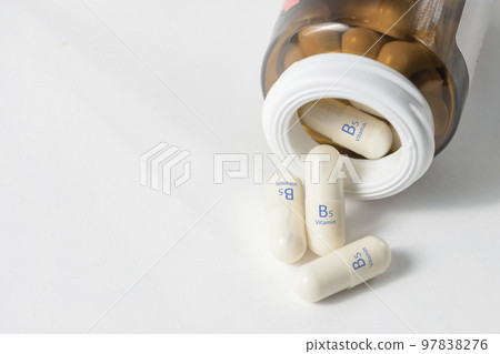 Vitamin B5. Pantothenic acid capsules play a role in the production of hormones and cholesterol. White capsules of vitamin B5 or panthenol are scattered on the table with copy space. 97838276