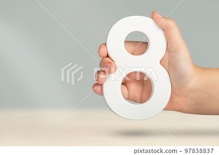 Eight in hand. A hand holds a white number 8 on a blurred background. Concept with number eight. Birthday 8 years, percentage, eighth grade or day, international women's day. Eight in hand. A hand holds a white number 8 on a blurred background. Concept with number eight. Birthday 8 years, percentage, eighth grade or day, international women's day. 97838837