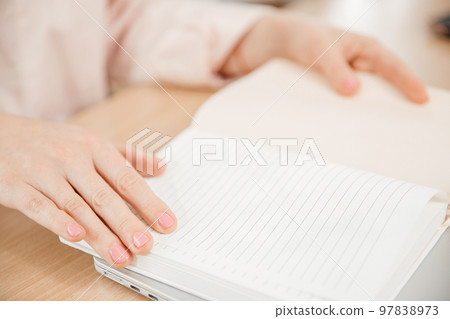 Close up of a woman's hands writing in a notepad placed on a wooden table, home office and work concept, plans and thoughts Close up of a woman's hands writing in a notepad placed on a wooden table, home office and work concept, plans and thoughts 97838973