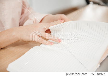 Close up of a woman's hands writing in a notepad placed on a wooden table, home office and work concept, plans and thoughts 97838974