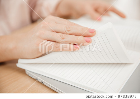 Close up of a woman's hands writing in a notepad placed on a wooden table, home office and work concept, plans and thoughts Close up of a woman's hands writing in a notepad placed on a wooden table, home office and work concept, plans and thoughts 97838975