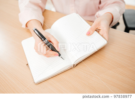 Close up of a woman's hands writing in a notepad placed on a wooden table, home office and work concept, plans and forecasts Close up of a woman's hands writing in a notepad placed on a wooden table, home office and work concept, plans and forecasts 97838977
