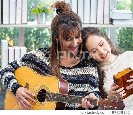 Young Asian lesbian couple intending to play a musical instrument together, guitar and kalimba, in the living room at home, the lifestyle of couple LGBT loving women happy in romantic love and fun Young Asian lesbian couple intending to play a musical instrument together, guitar and kalimba, in the living room at home, the lifestyle of couple LGBT loving women happy in romantic love and fun 97839103