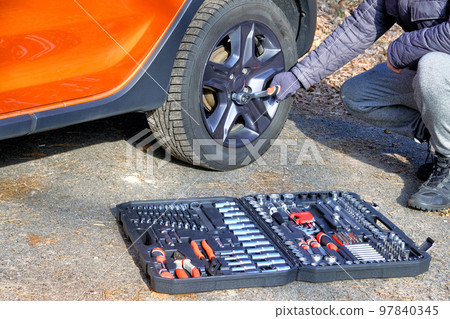 Car driver using different repair tools for repairing a car. Tool set in box near the orange auto. Automobile maintenance concept. 97840345