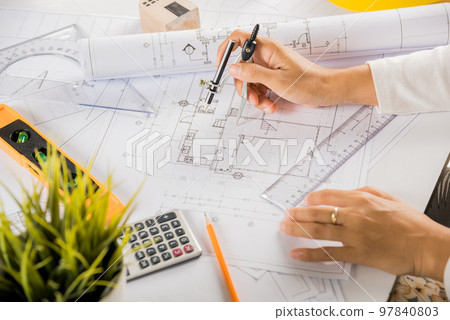 Architectural project workplace. Architect drawing with divider compass on house plan blueprint paper for repair tools on table desk at architecture office, Engineer sketching construction project Architectural project workplace. Architect drawing with divider compass on house plan blueprint paper for repair tools on table desk at architecture office, Engineer sketching construction project 97840803
