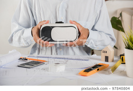 Architectural building design holding 3D VR glasses and construction plans with blueprints paper project plans, designing man edit building or architecture, technology industry, Architect workplace Architectural building design holding 3D VR glasses and construction plans with blueprints paper project plans, designing man edit building or architecture, technology industry, Architect workplace 97840804