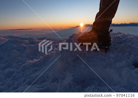 Man climbs a mountain peak in winter during sunrise. A shoe with spikes on - crampons.  97841116