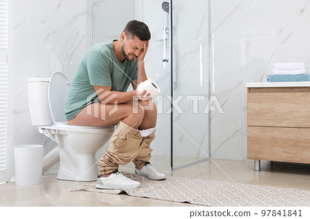 Man suffering from hemorrhoid on toilet bowl in rest room 97841841