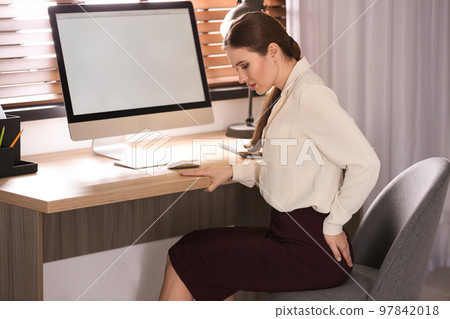 Young woman suffering from hemorrhoid at workplace in office 97842018