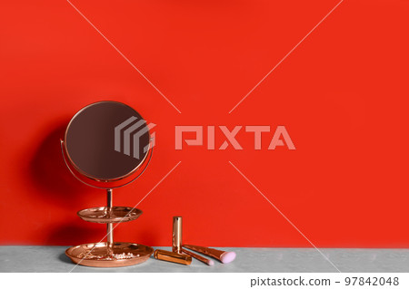 Small mirror and makeup products on grey marble table near red wall. Space for text Small mirror and makeup products on grey marble table near red wall. Space for text 97842048