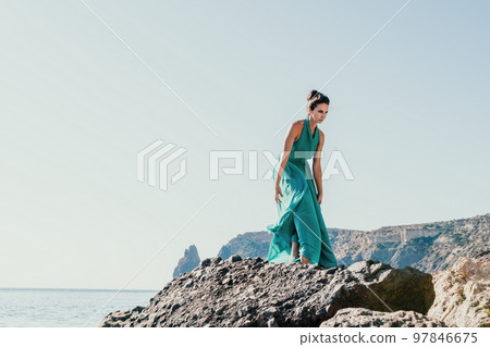 Side view a Young beautiful sensual woman with black hair in a long mint dress posing on a beach with calm sea bokeh lights on sunny day. Girl on the nature on blue sky background. Fashion photo Side view a Young beautiful sensual woman with black hair in a long mint dress posing on a beach with calm sea bokeh lights on sunny day. Girl on the nature on blue sky background. Fashion photo 97846675