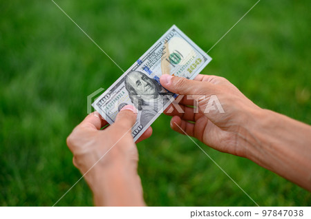 Close up 100 Dollar bank note in hand on grass background. One hundred American dollars. Close up 100 Dollar bank note in hand on grass background. One hundred American dollars. 97847038