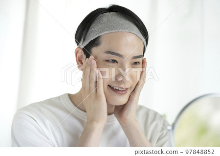 Young man touching his cheek while looking in the mirror Skin care image 97848852