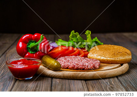Front view of process of making burger with vegetables, bun and artificial meat on wooden board Front view of process of making burger with vegetables, bun and artificial meat on wooden board 97852733
