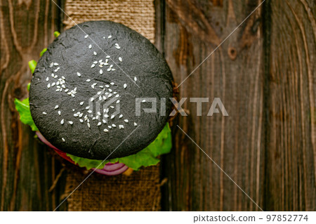 Top down view of black burger with meat cutlet and vegetables on rustic wooden table. Copy Space  97852774