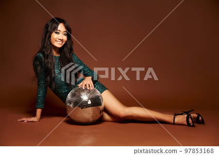 Pretty woman in sequin party gown posing on floor with disco ball 97853168