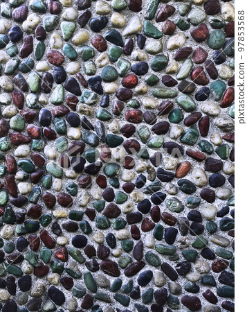 Vertical background image of a wall with embedded pebbles in turquoise, brown, black and white under weak sunlight 97853568
