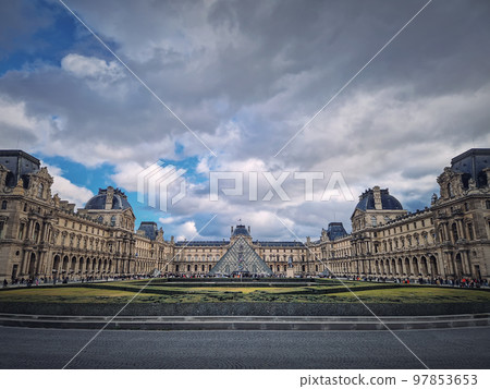 Outdoors view to the Louvre Museum in Paris, France. The historical palace building with the modern glass pyramid in center Outdoors view to the Louvre Museum in Paris, France. The historical palace building with the modern glass pyramid in center 97853653