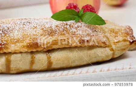 Baked strudel with apples sprinkled with powdered sugar on a white wooden board, delicious dessert 97853978