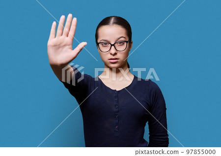 Serious confident teenage girl looking at camera making stop gesture with palm 97855000