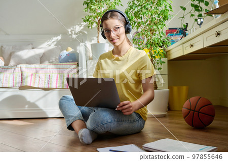 Teenage girl with headphones studying at home using a laptop Teenage girl with headphones studying at home using a laptop 97855646