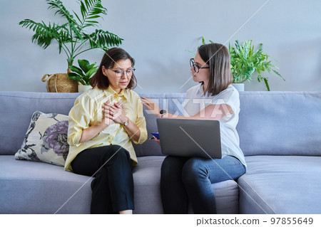 Female psychologist and middle aged woman patient sitting together on couch in office Female psychologist and middle aged woman patient sitting together on couch in office 97855649