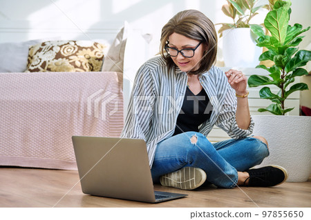 Mature woman sitting on the floor at home looking at laptop 97855650