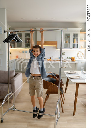 Little preteen boy child hanging on clothes hanger Little preteen boy child hanging on clothes hanger 97857323