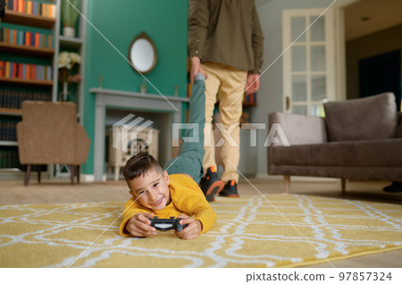 Portrait of smiling son playing video game while father pulling him out 97857324