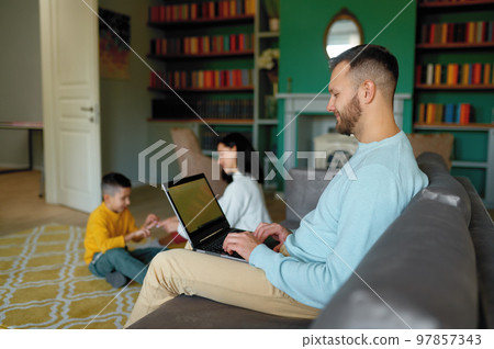 Man working on laptop while his family playing together Man working on laptop while his family playing together 97857343