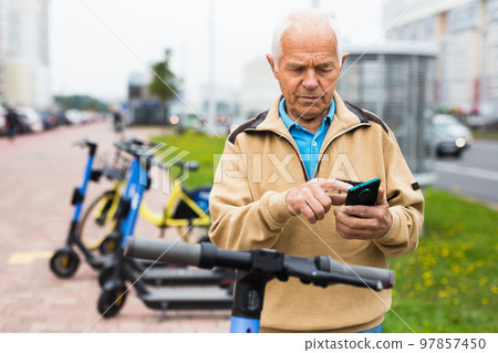 Senior man with smartphone activating electric scooter 97857450
