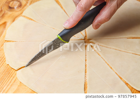 A womans hand cuts the dough with a kitchen knife A womans hand cuts the dough with a kitchen knife 97857945