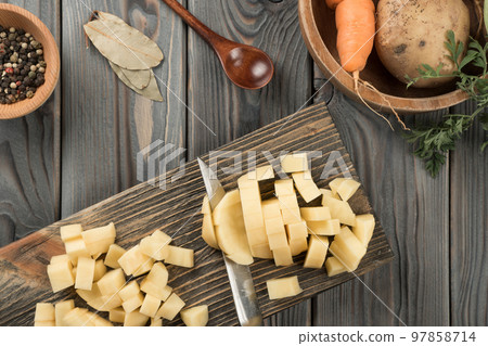 Cutting into cubes with knife raw yellow potato on kitchen wooden board. Fresh diced potato, traditional cuisine. Cutting into cubes with knife raw yellow potato on kitchen wooden board. Fresh diced potato, traditional cuisine. 97858714