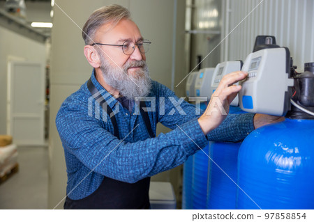 Bearded mature man controlling machinery in a brewery Bearded mature man controlling machinery in a brewery 97858854