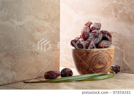Dates fruit in a wooden dish on a beige ceramic table. 97859281