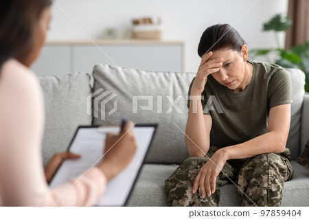 Military psychiatry concept. Depressed soldier lady sitting on couch during therapy session 97859404